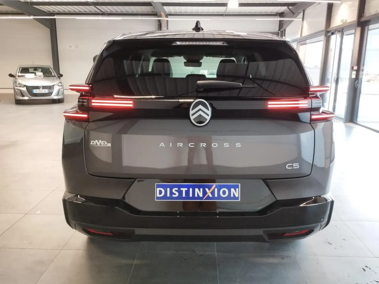 Vue arrière d'un Citroën C5 Aircross gris platine avec feux arrière LED horizontaux allumés en intérieur showroom.