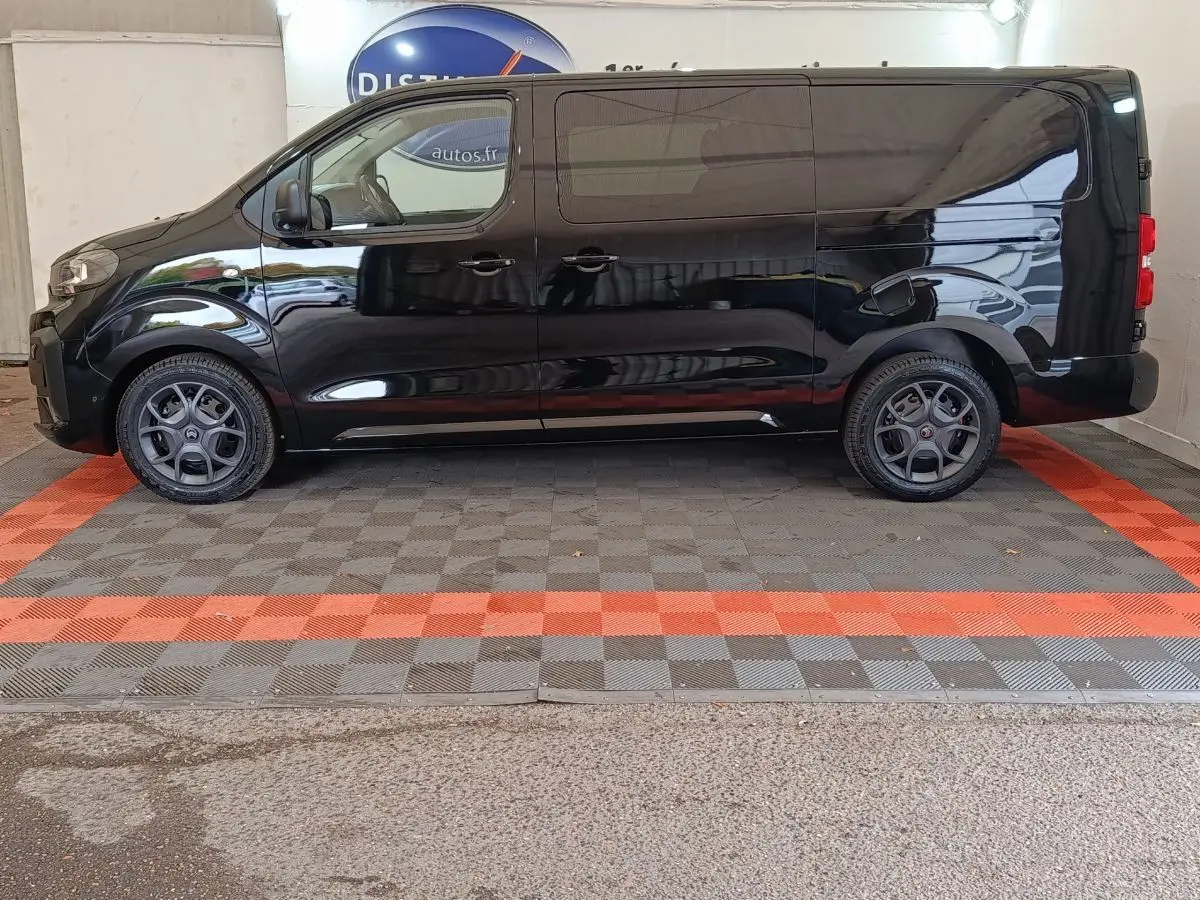 Profil côté gauche d'un Citroën Jumpy XL noir 2025 avec jantes spécifiques et vitres teintées en intérieur showroom.