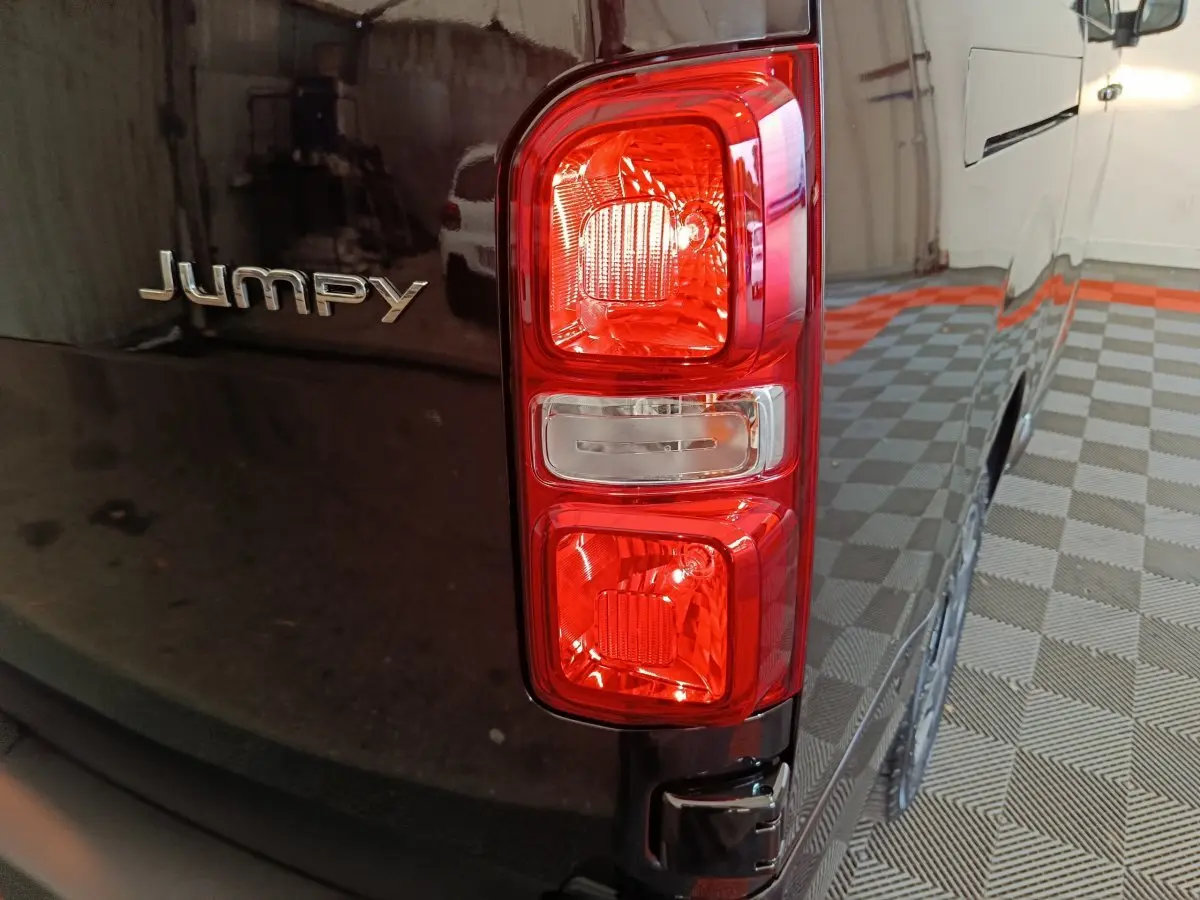 Gros plan sur le feu arrière droit et le logo Jumpy d’un Citroën Jumpy XL noir stationné en intérieur.