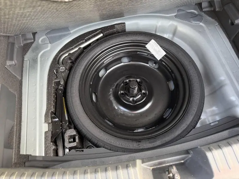 Vue plongeante sur la roue de secours noire et le cric dans le coffre d'une SEAT LEON 1.5 eTSI Hybrid 2025 gris métallique.