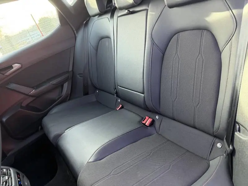 Vue intérieure côté gauche des sièges arrière en tissu noir du SEAT LEON 1.5 eTSI Hybrid 2025 avec ceintures de sécurité visibles.