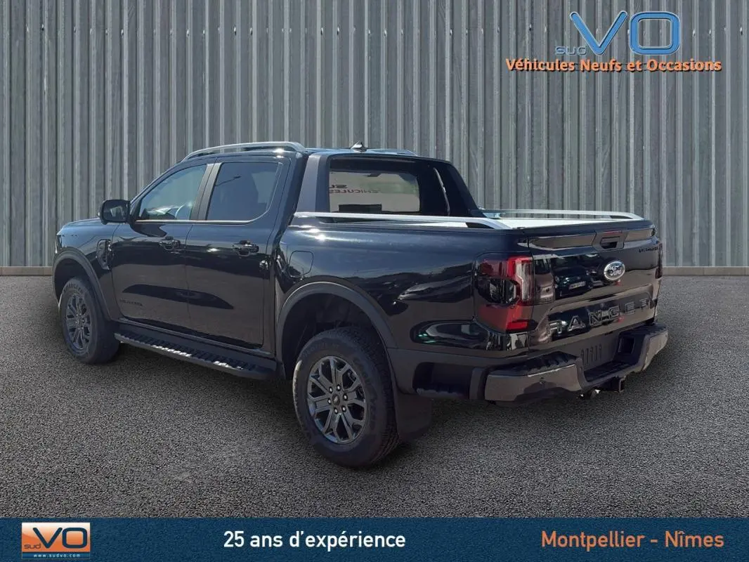 Ford Ranger Wildtrak noir vu en 3/4 arrière droit, avec barres de toit, marchepieds et vitres surteintées.