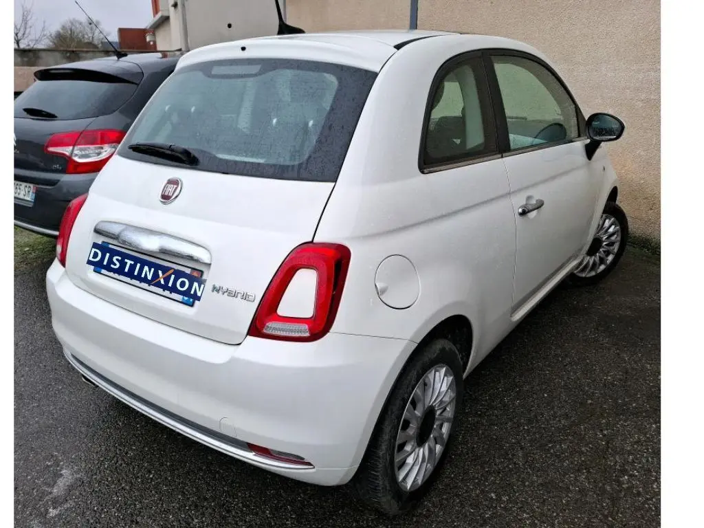 Vue 3/4 arrière droite d'une Fiat 500 blanche Bossa Nova avec logo Hybrid visible sur un parking.