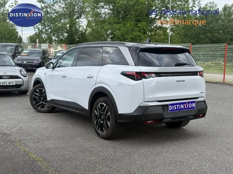 Peugeot 5008 Hybrid blanc Okénite vue 3/4 arrière droit, jantes noires et vitres teintées, stationné en extérieur.