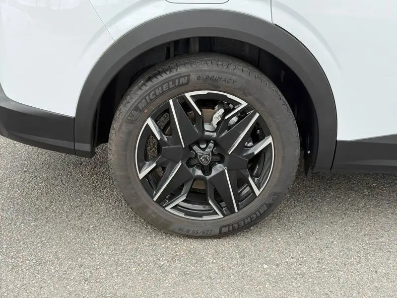 Gros plan sur la roue avant droite du Peugeot 5008 Hybrid blanc Okénite, avec jante noire et détails argentés.
