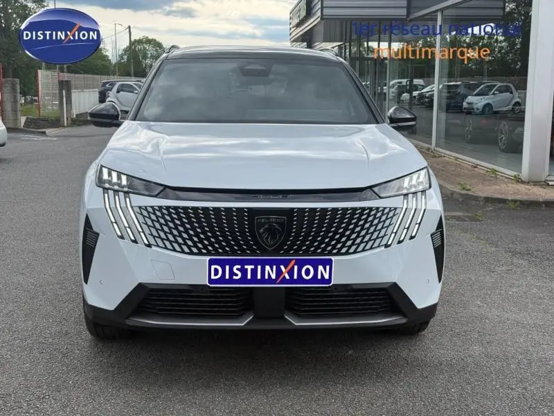 Vue de face d’un Peugeot 5008 Hybrid blanc Okénite avec calandre noire à motif géométrique et feux LED verticaux distinctifs.
