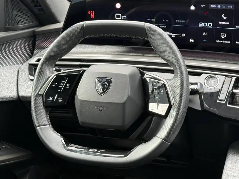 Vue rapprochée du volant multifonction du Peugeot 5008 Hybrid 145ch GT, avec tableau de bord numérique en arrière-plan.