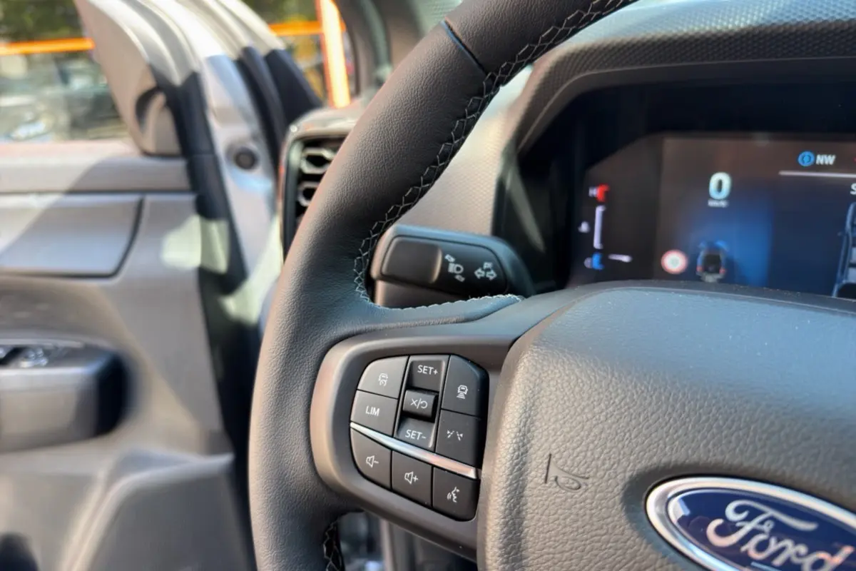 Gros plan sur le volant cuir multifonctions du Ford Ranger gris iconic, avec tableau de bord numérique en arrière-plan.