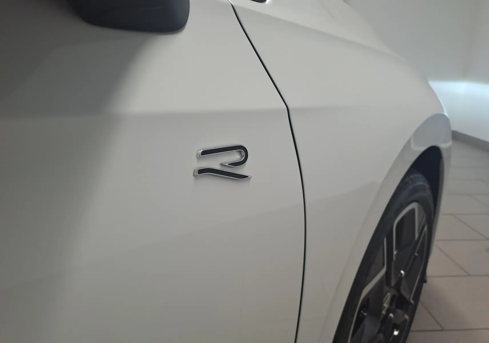 Détail de l’emblème R sur l’aile avant droite d’une Volkswagen Golf blanc Oryx nacré avec jante noire.