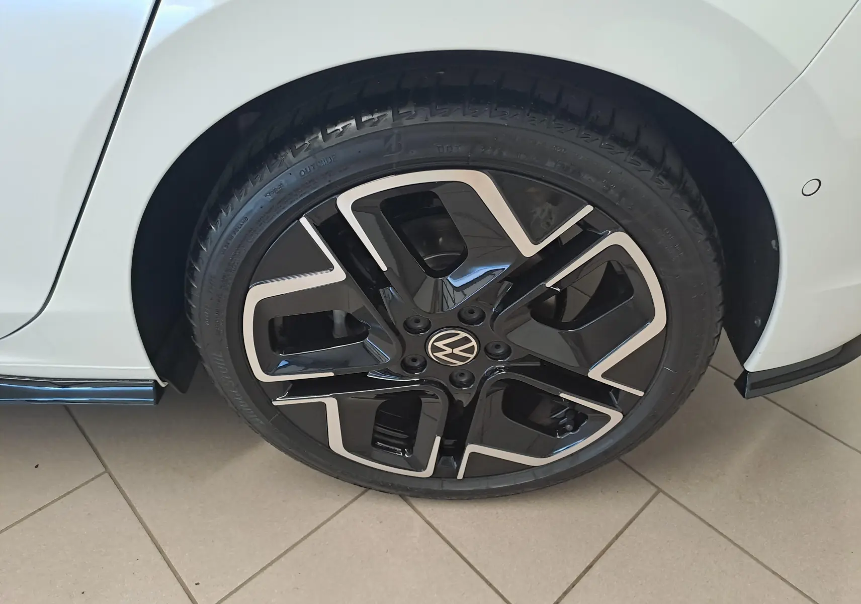 Gros plan sur la roue avant gauche d’une Volkswagen Golf blanche avec jante noire et argentée au design moderne.