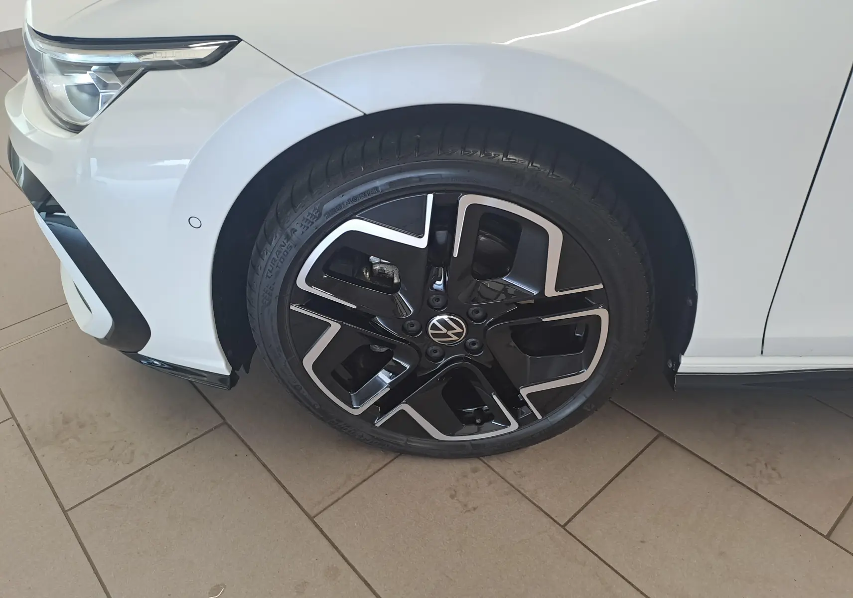 Gros plan sur la roue avant gauche d'une Volkswagen Golf blanche nacrée avec jante noire et argentée au design moderne.