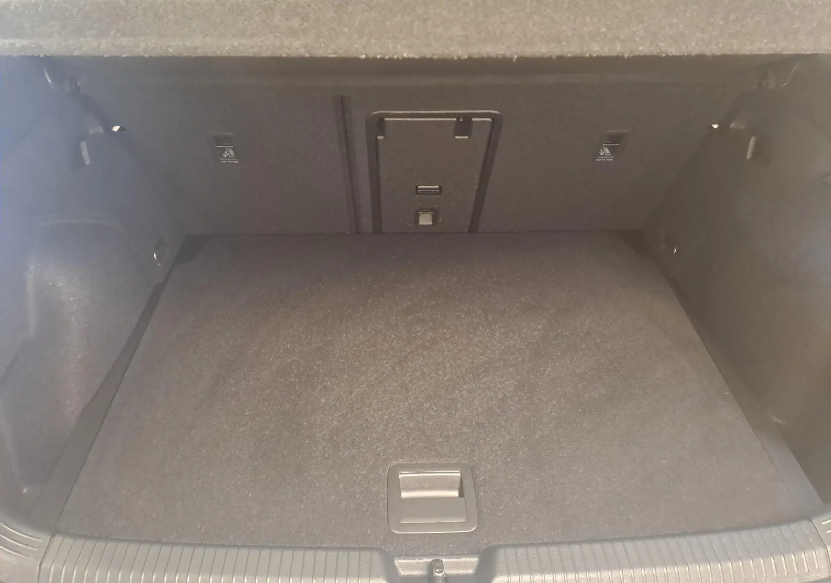 Vue intérieure du coffre spacieux et propre de la Volkswagen Golf 2.0 TDI blanc Oryx, avec tapis de sol noir.