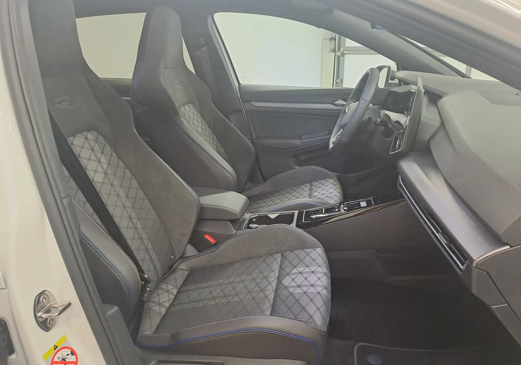 Vue intérieure côté conducteur de la Volkswagen Golf 2.0 TDI blanche, sièges sport en tissu et alcantara avec surpiqûres bleues.