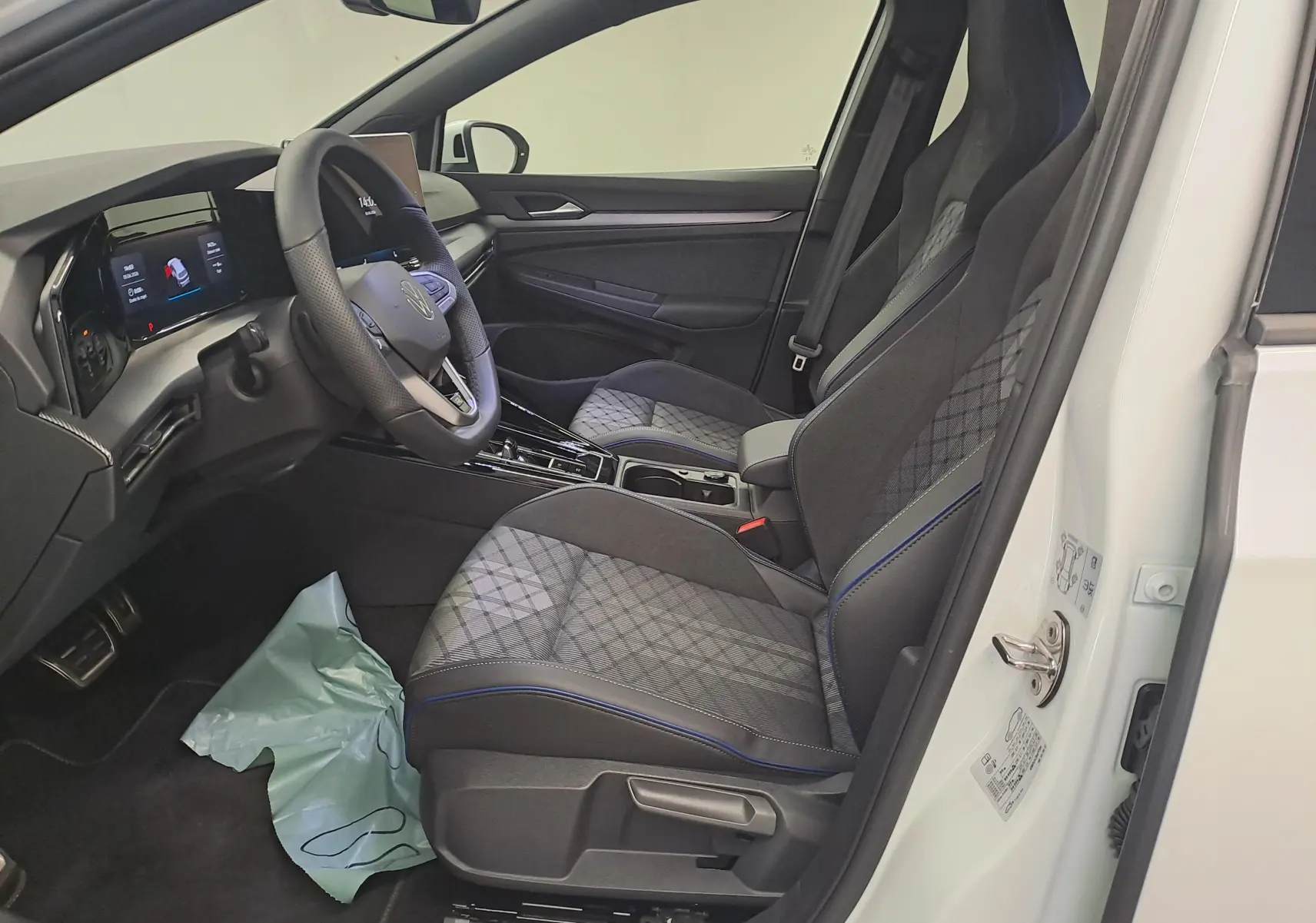 Vue intérieure côté conducteur de la Volkswagen Golf 2.0 TDI blanche, sièges tissu gris à surpiqûres bleues et volant cuir.