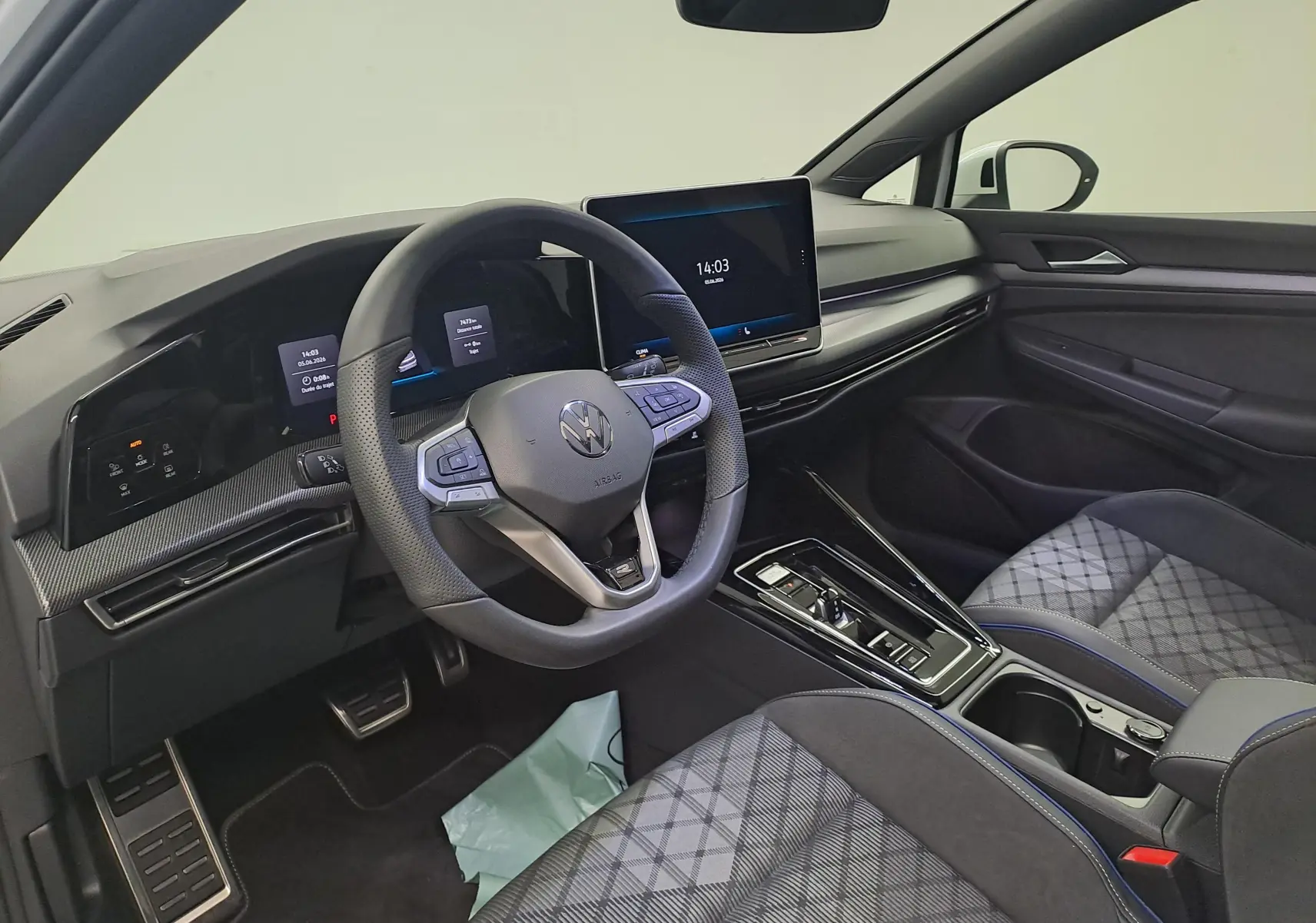 Vue intérieure côté conducteur de la Volkswagen Golf 2025 avec volant cuir, tableau de bord digital et sièges tissu gris à motifs.