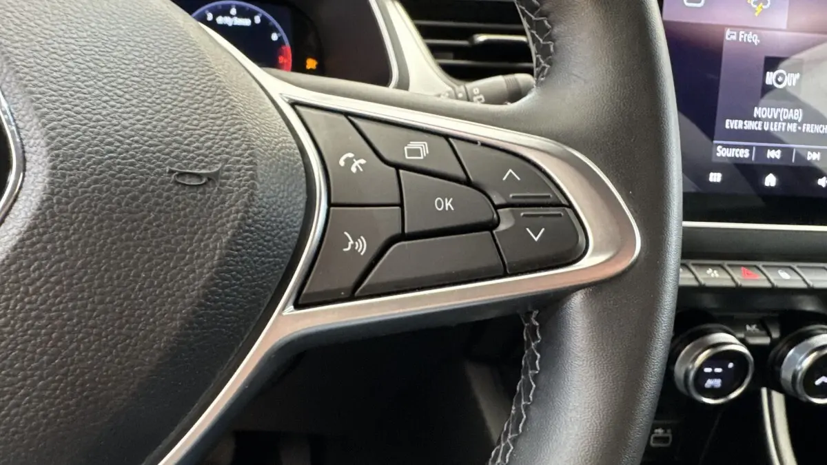 Gros plan sur les commandes au volant à droite du Renault Captur rouge 2024, avec écran tactile et tableau de bord partiel.