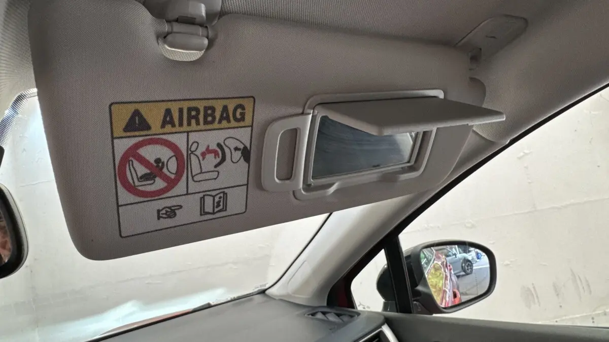 Vue intérieure côté conducteur du pare-soleil avec miroir et avertissement airbag, rétroviseur montrant la carrosserie rouge du Renault Captur.