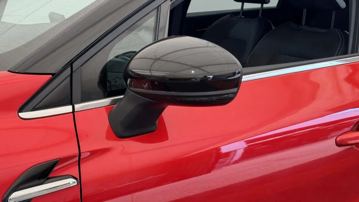 Gros plan sur le rétroviseur noir côté gauche d’un Renault Captur rouge 2024, avec fenêtre et partie de porte visibles.