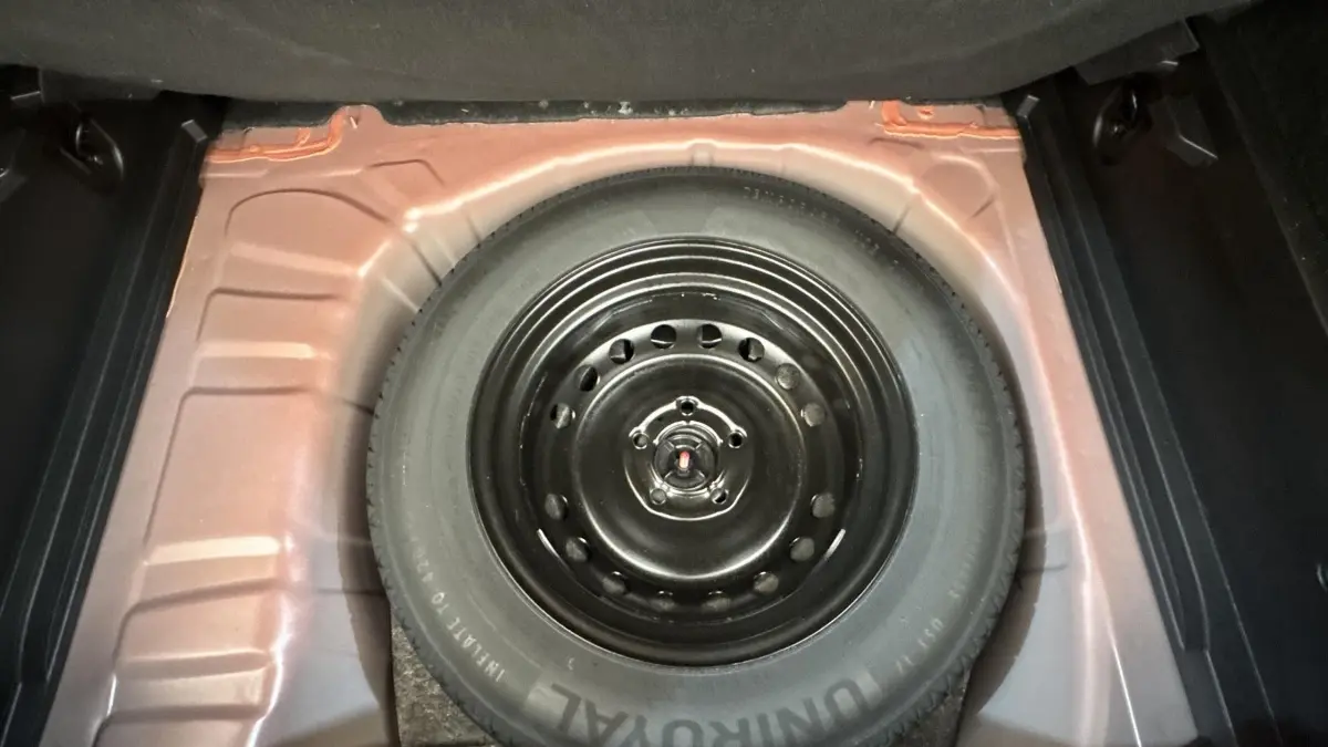 Vue en plongée sur la roue de secours noire dans le compartiment arrière du Renault Captur rouge 2024.