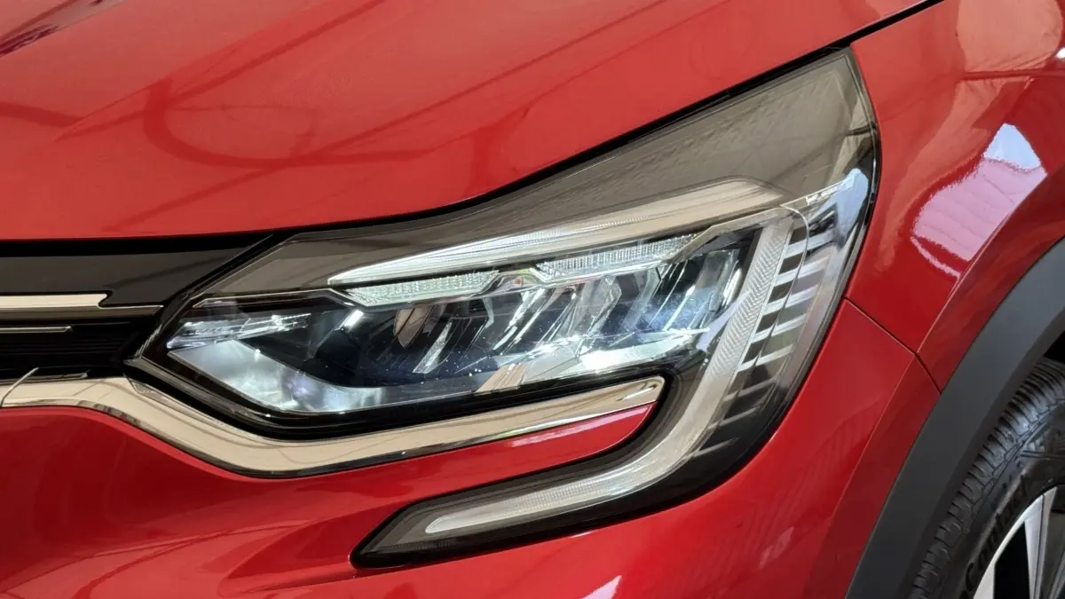 Gros plan sur le phare avant droit LED du Renault Captur rouge 2024 avec détails chromés et carrosserie brillante.