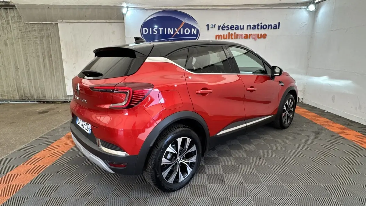Vue 3/4 arrière droite d'un Renault Captur rouge 2024 avec toit noir et jantes alliage bicolores dans un garage.