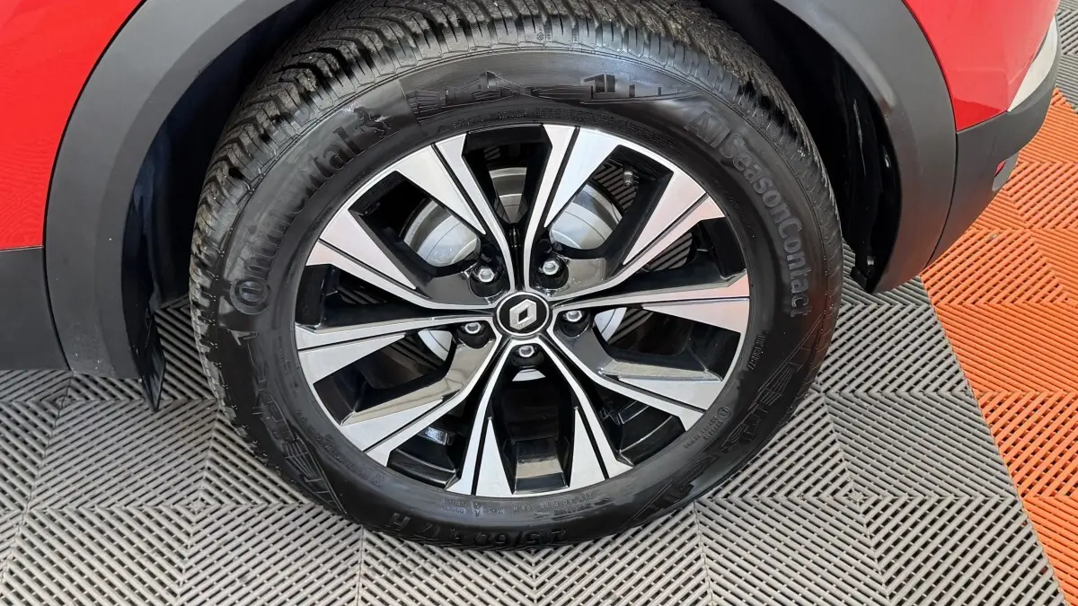 Gros plan sur la roue avant droite du Renault Captur rouge 2024 avec jante alliage bicolore et logo Renault central.