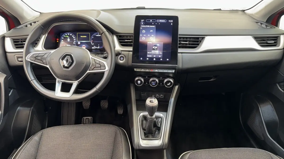 Vue intérieure avant du tableau de bord noir et gris du Renault Captur rouge 2024 avec écran tactile vertical et boîte manuelle.