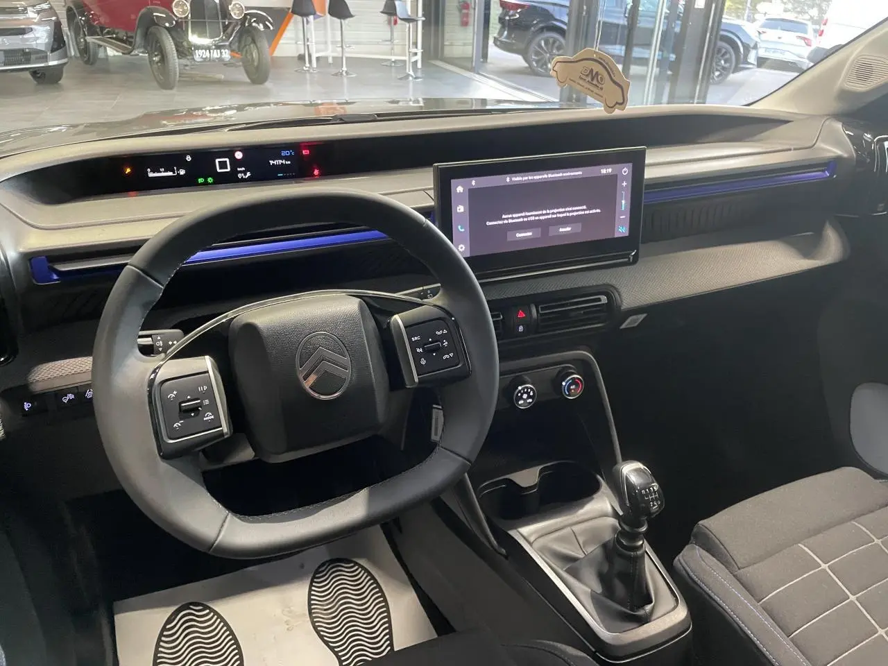 Intérieur de Citroën C3 2025 vu côté conducteur, volant multifonctions, écran tactile 10,25" et levier de vitesse manuel.