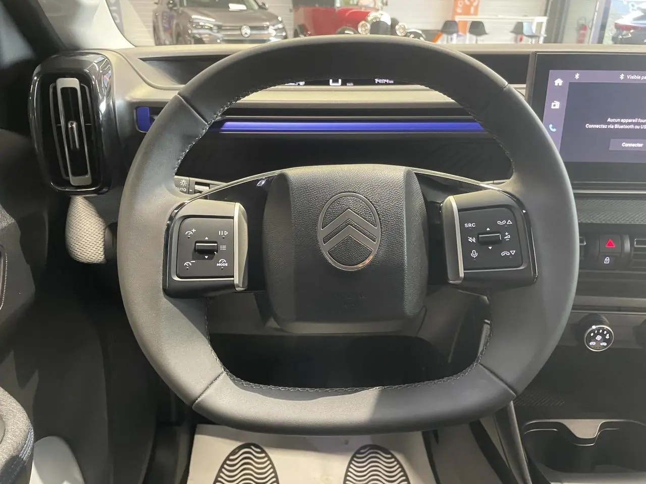 Vue rapprochée du volant noir gainé de la Citroën C3 2025 avec commandes intégrées et tableau de bord gris et bleu.