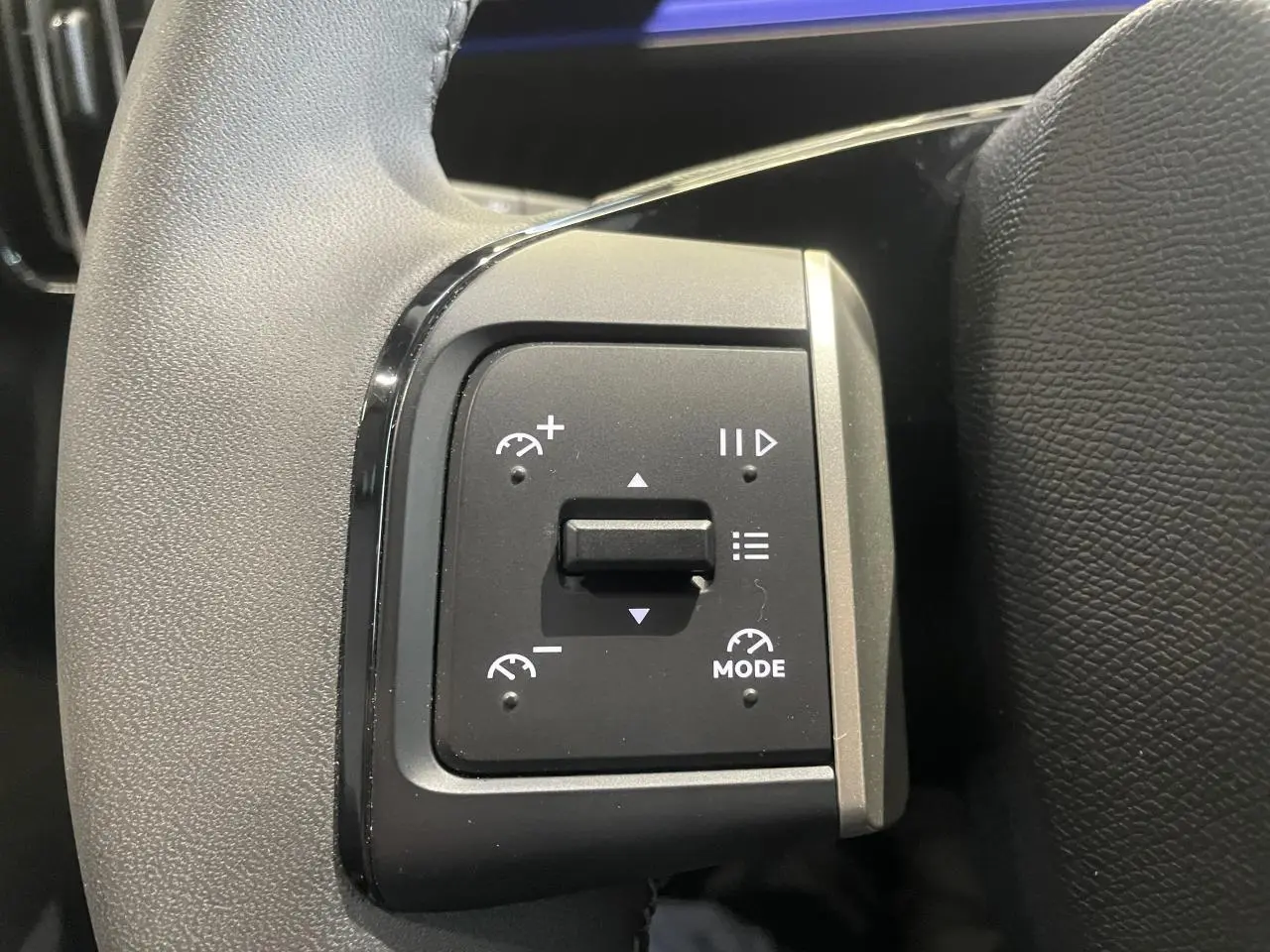 Gros plan sur les commandes de régulateur de vitesse au volant cuir noir de la Citroën C3 gris foncé.