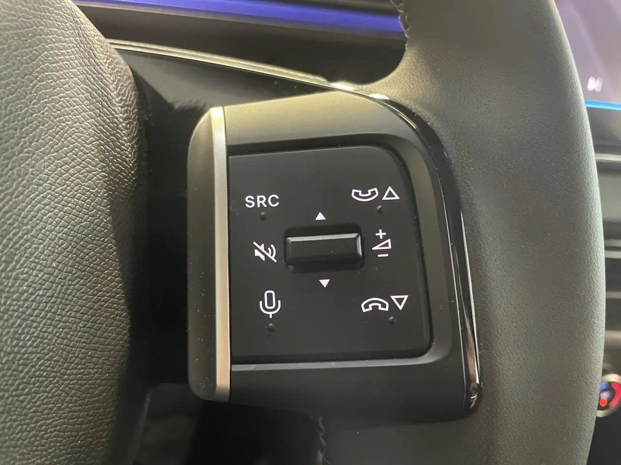 Gros plan sur les commandes multifonctions noires à gauche du volant gainé d'une Citroën C3 gris foncé 2025.