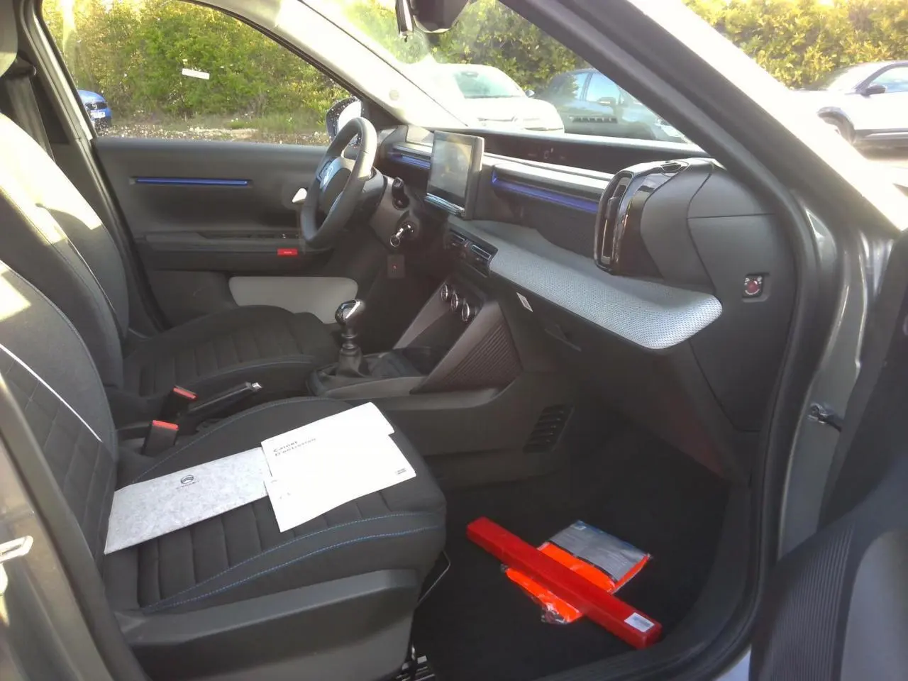 Vue intérieure côté passager avant de la Citroën C3 2025 gris foncé, avec sièges tissu noir et décor bleu sur la planche de bord.