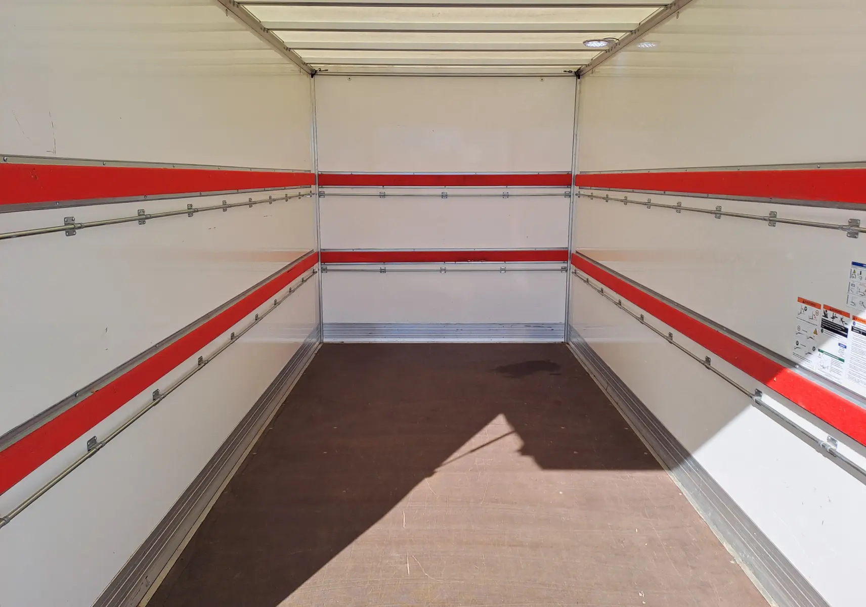 Intérieur vide du coffre d’un Nissan Interstar châssis cabine blanc, vue de l’arrière vers l’avant avec bandes rouges sur les parois.