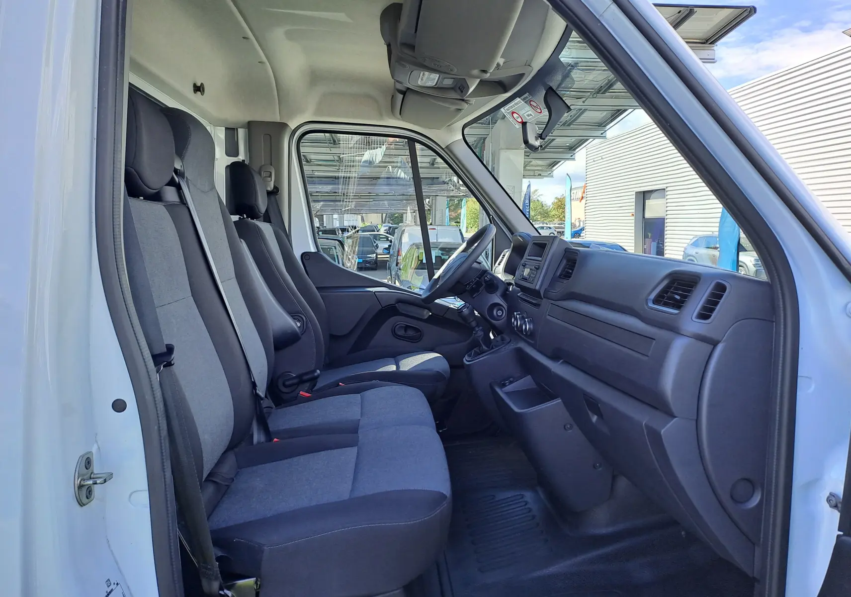 Vue intérieure côté conducteur du Nissan Interstar blanc 2024, montrant les sièges gris et le tableau de bord fonctionnel.
