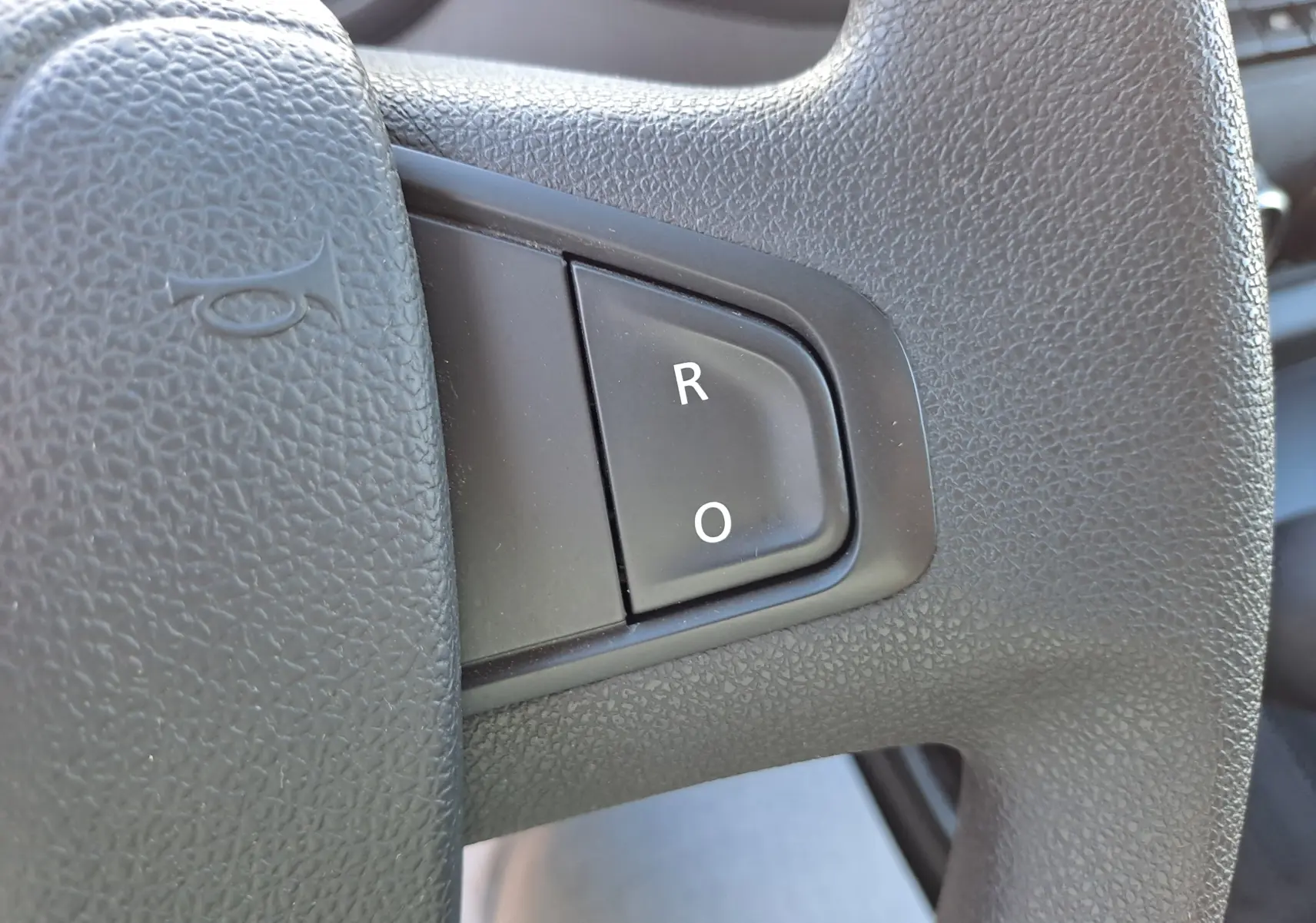 Gros plan sur le bouton de commande noir marqué "R" et "O" sur le volant texturé du Nissan Interstar blanc 2024.