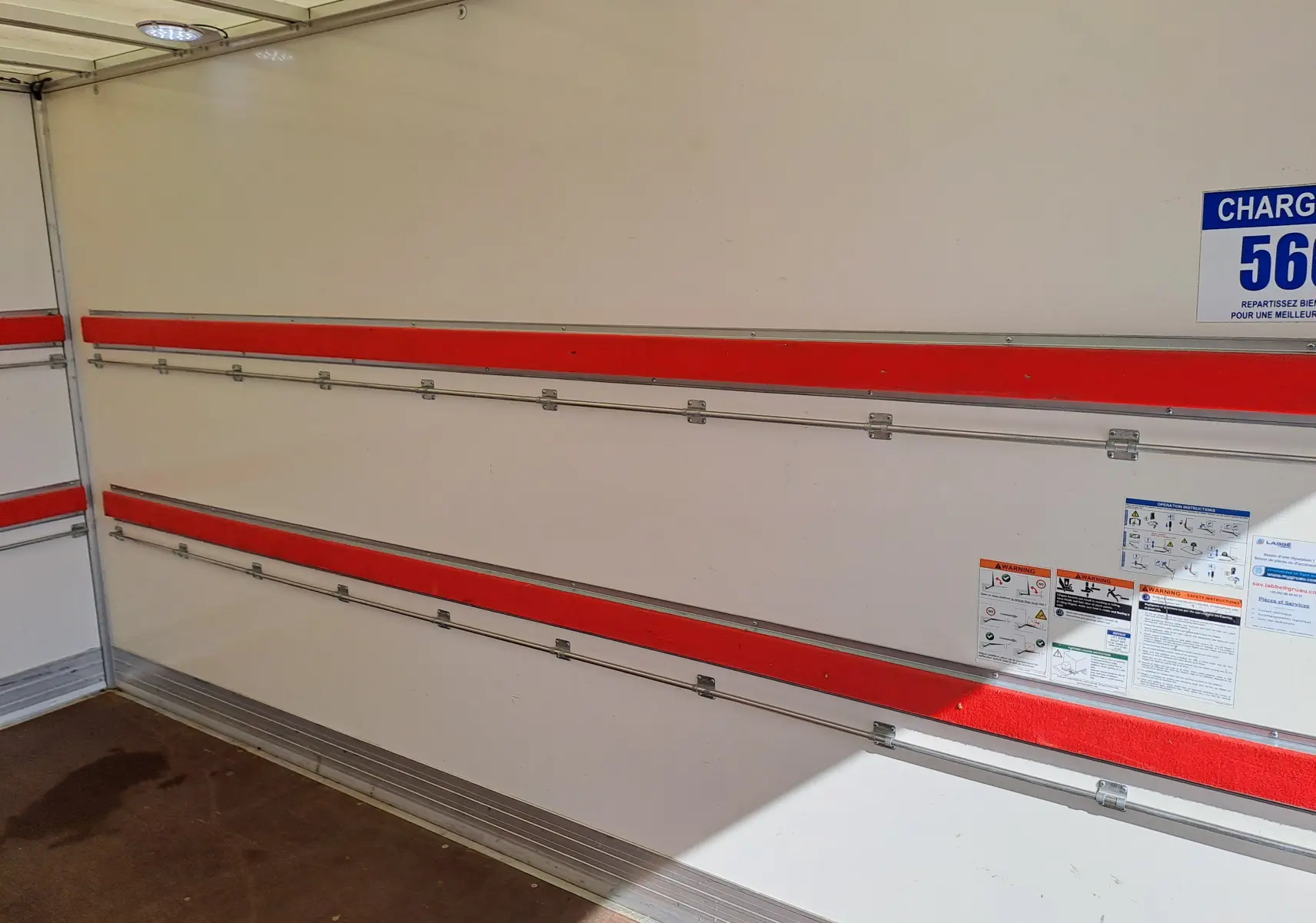 Intérieur de la benne d’un Nissan Interstar blanc, vue latérale droite avec rails rouges et panneaux d’avertissement.