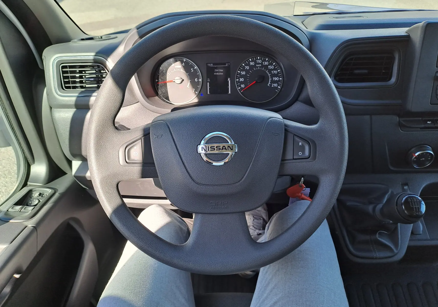 Vue intérieure centrée sur le volant Nissan d’un Interstar blanc 2024 avec tableau de bord et levier de vitesse manuel visible.