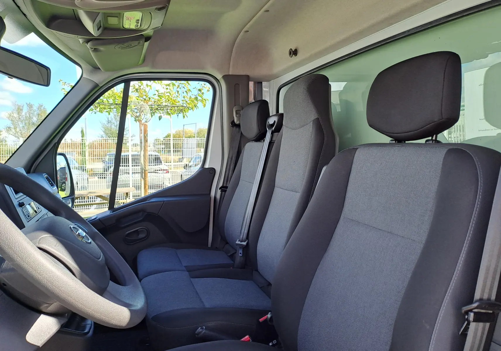 Vue intérieure côté conducteur du Nissan Interstar blanc 2024, montrant les sièges tissu gris et noir et le volant.