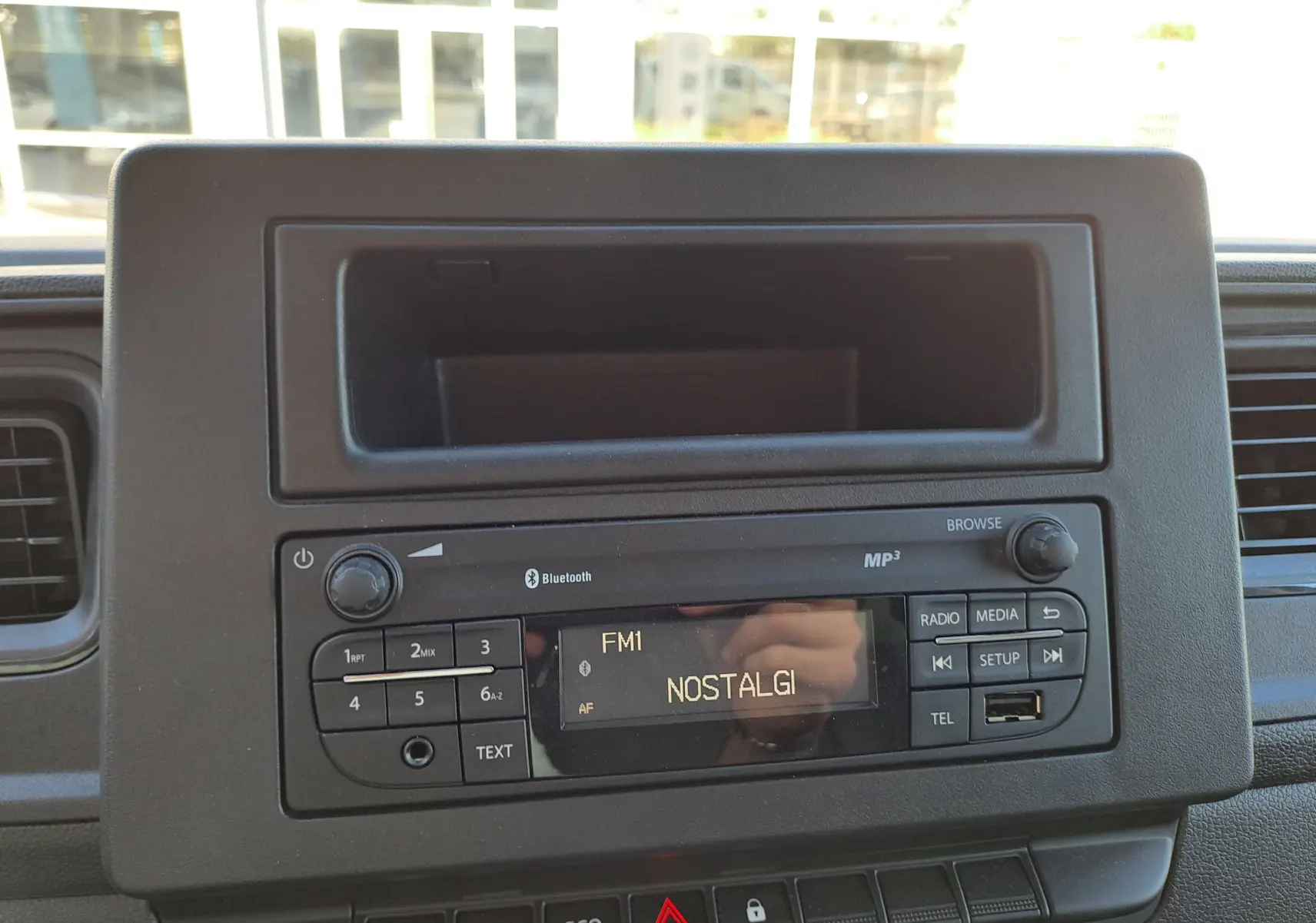 Vue rapprochée de la radio Bluetooth noire intégrée au tableau de bord du Nissan Interstar blanc, affichant la station FM1 NOSTALGI.