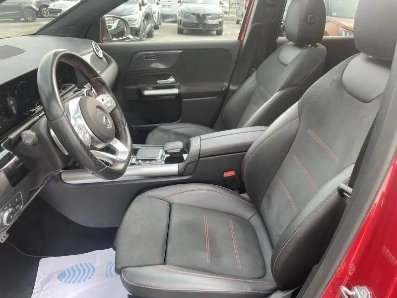 Intérieur du Mercedes GLA 200 D AMG-LINE 2022 en rouge métal, vue côté conducteur avec sièges en cuir noir et surpiqûres rouges.