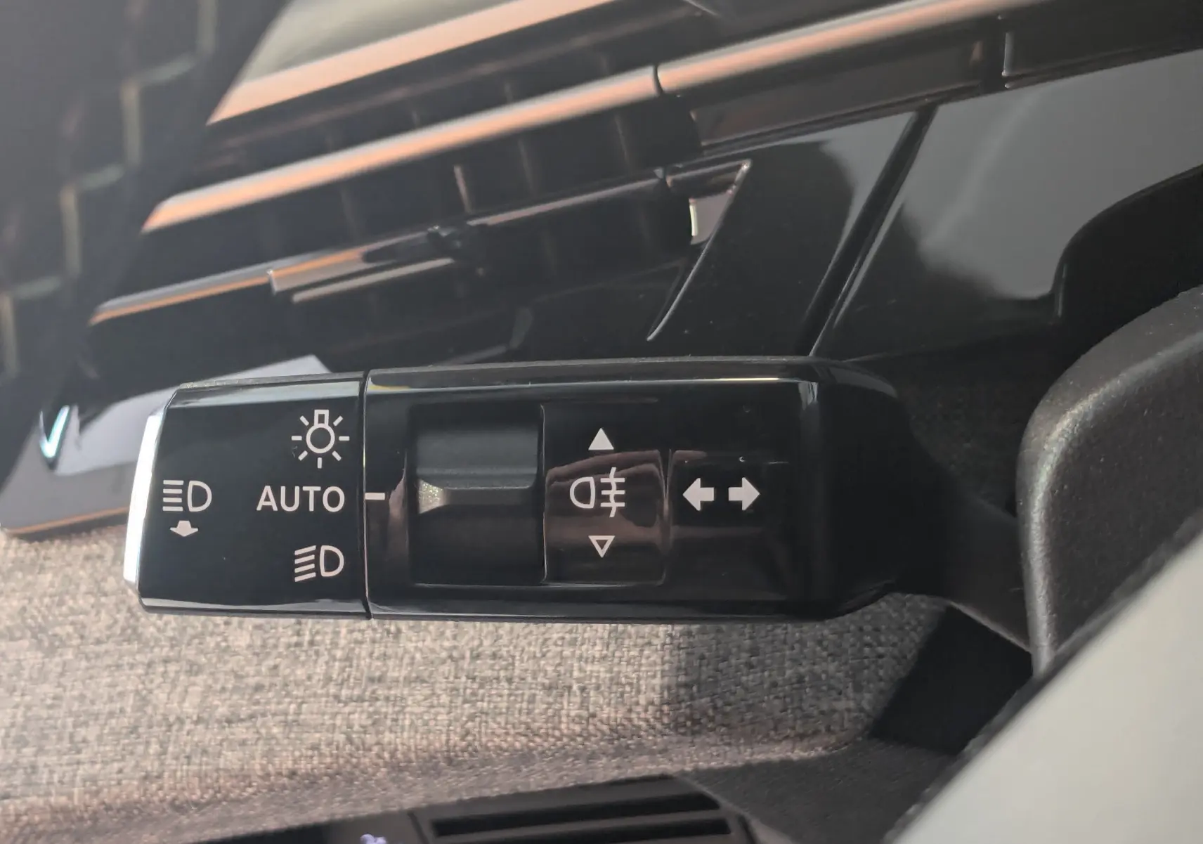 Gros plan sur la commande des feux et clignotants du Peugeot 3008 Hybrid 145 gris titane, intérieur tissu gris.