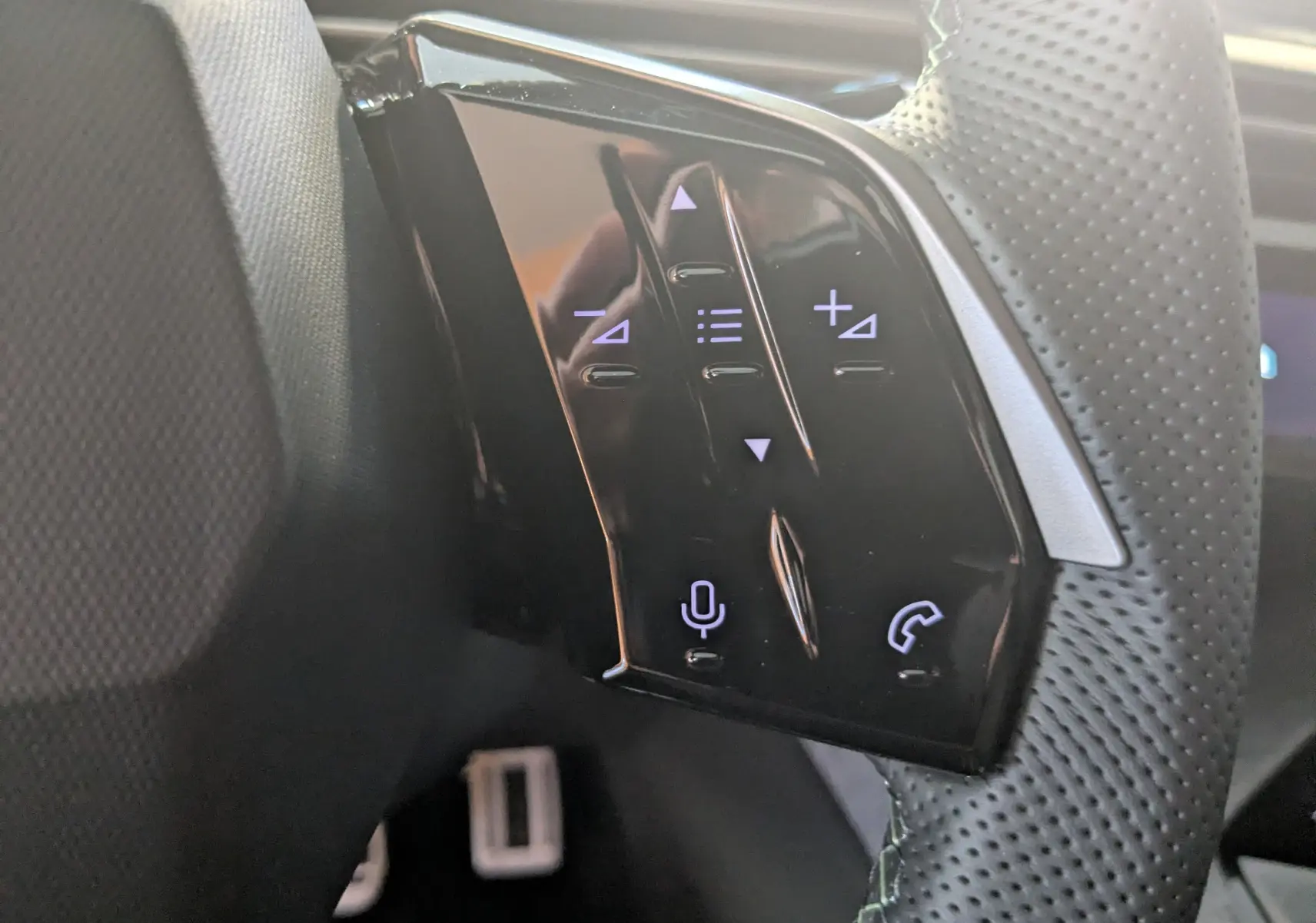 Gros plan sur les commandes tactiles noires du volant perforé côté gauche du Peugeot 3008 Hybrid 145 GT gris titane.