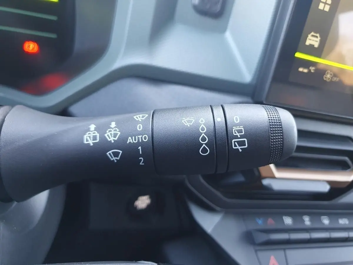 Gros plan sur la commande d’essuie-glace du Dacia Duster gris schiste, avec tableau de bord et écran tactile en arrière-plan.
