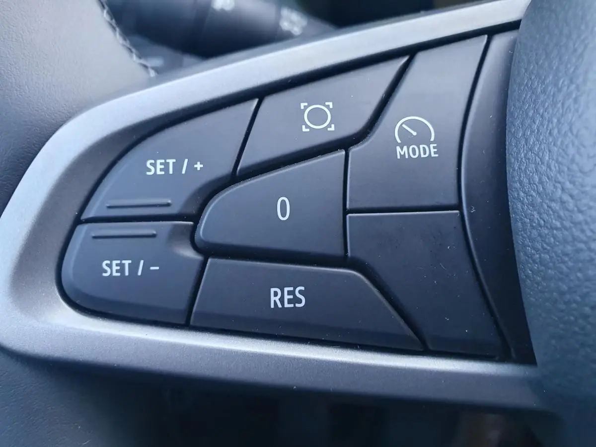 Gros plan sur les commandes noires du volant du Dacia Duster 2026, avec boutons de régulateur de vitesse et mode.