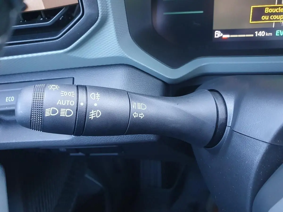 Gros plan sur la commande des feux et clignotants du Dacia Duster 2026 gris schiste, avec affichage digital partiel.