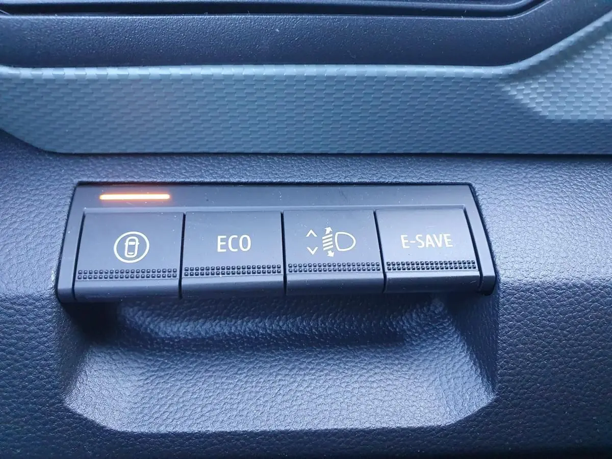 Gros plan sur les boutons de commande du tableau de bord du Dacia Duster gris schiste, avec témoin lumineux orange.