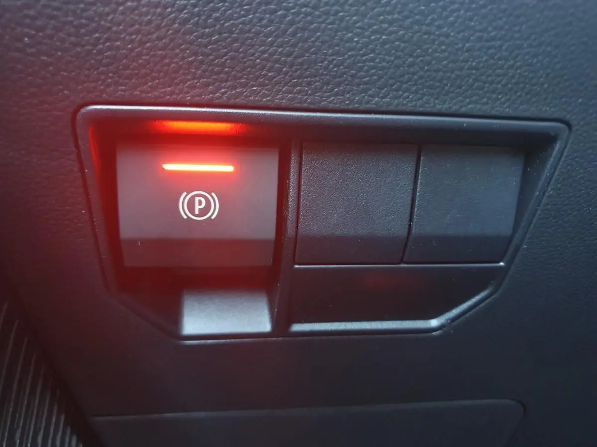 Gros plan sur le bouton de frein de stationnement électronique illuminé en rouge dans l'habitacle du Dacia Duster gris schiste.