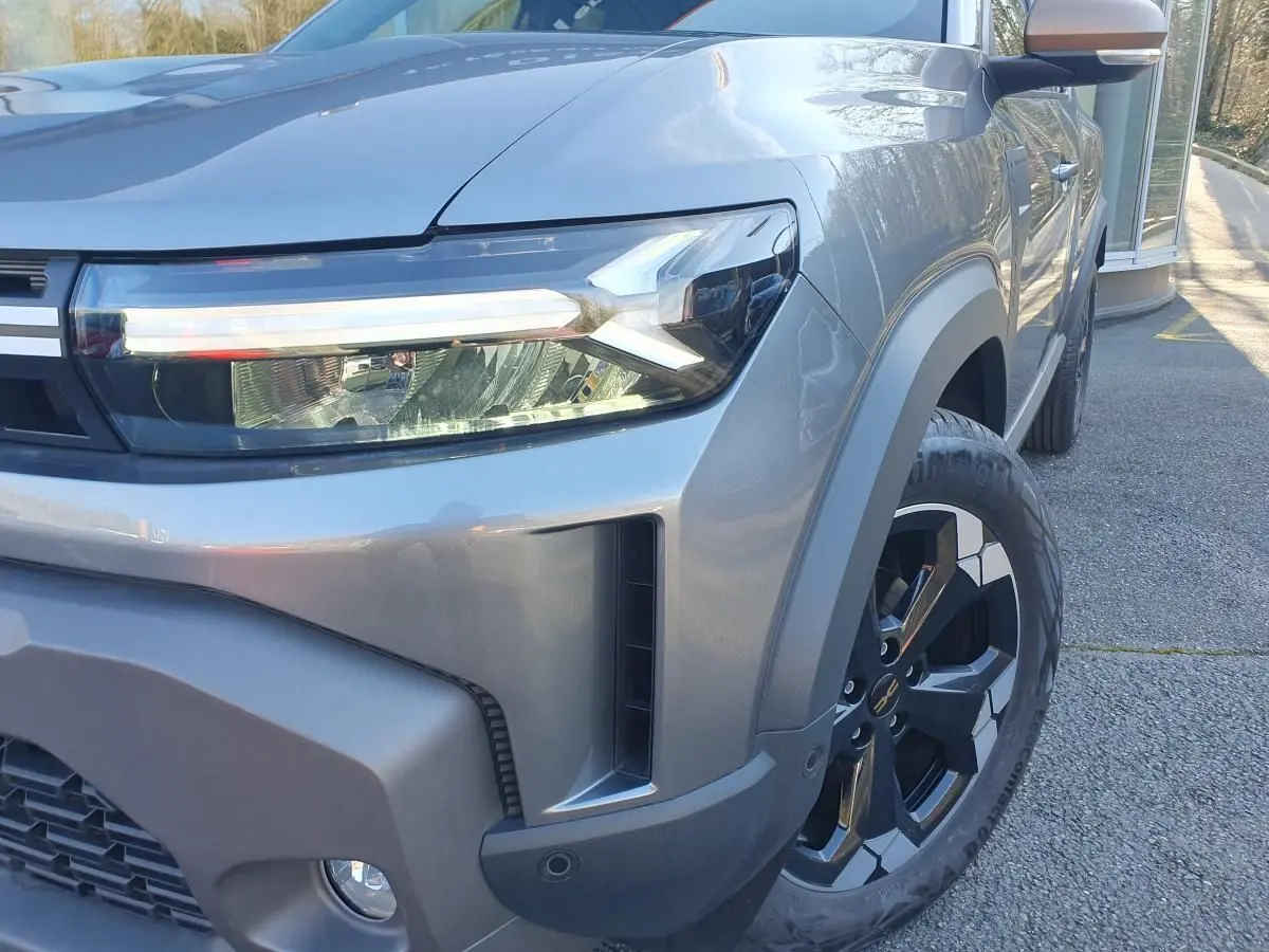 Gros plan sur l'avant droit du Dacia Duster gris schiste, mettant en valeur le phare LED et la jante alliage 17 pouces.