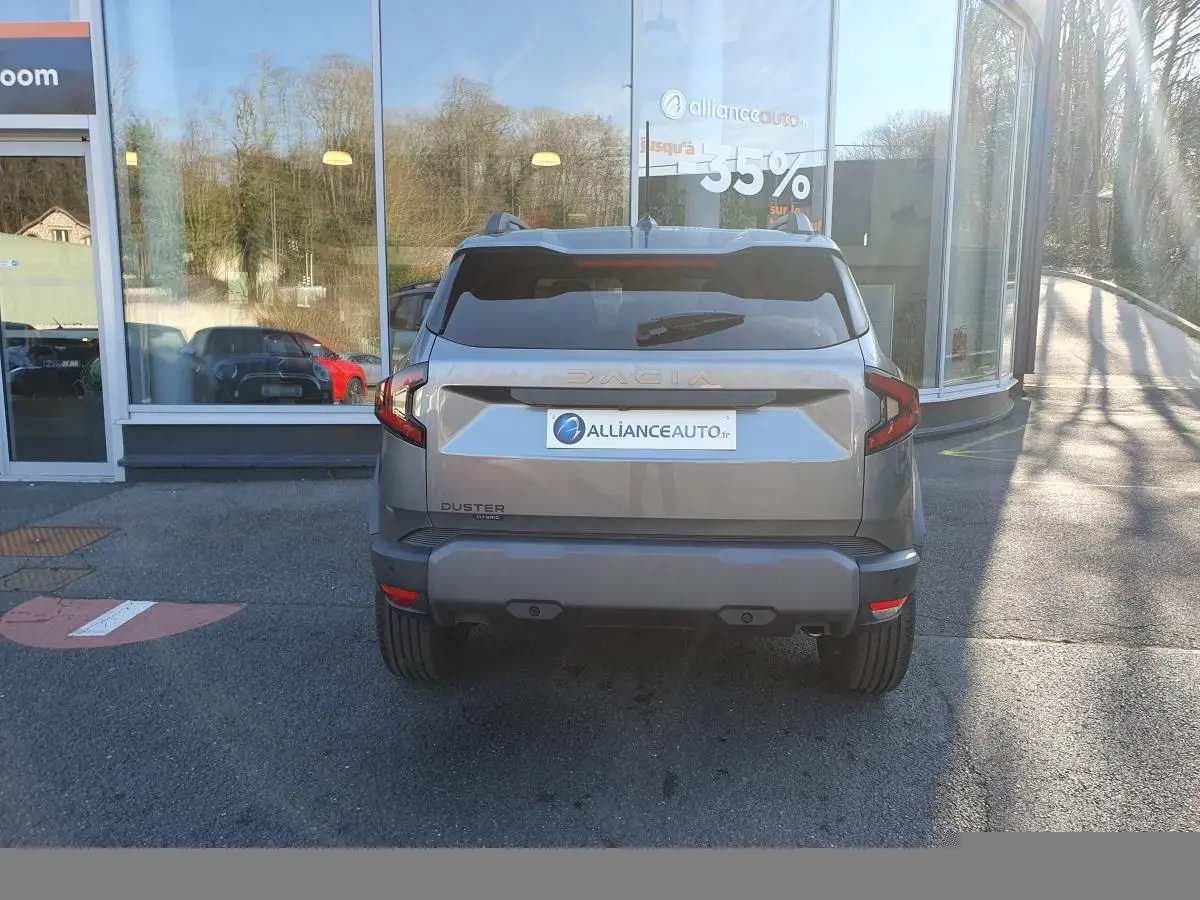 Vue arrière d'un Dacia Duster gris schiste 2026 avec logo Dacia lumineux et feux arrière LED distinctifs.