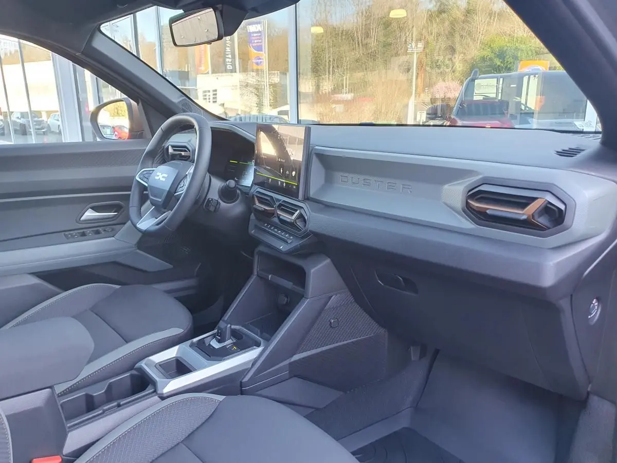 Vue intérieure côté conducteur du Dacia Duster 2026 gris schiste, avec tableau de bord moderne et écran tactile central.